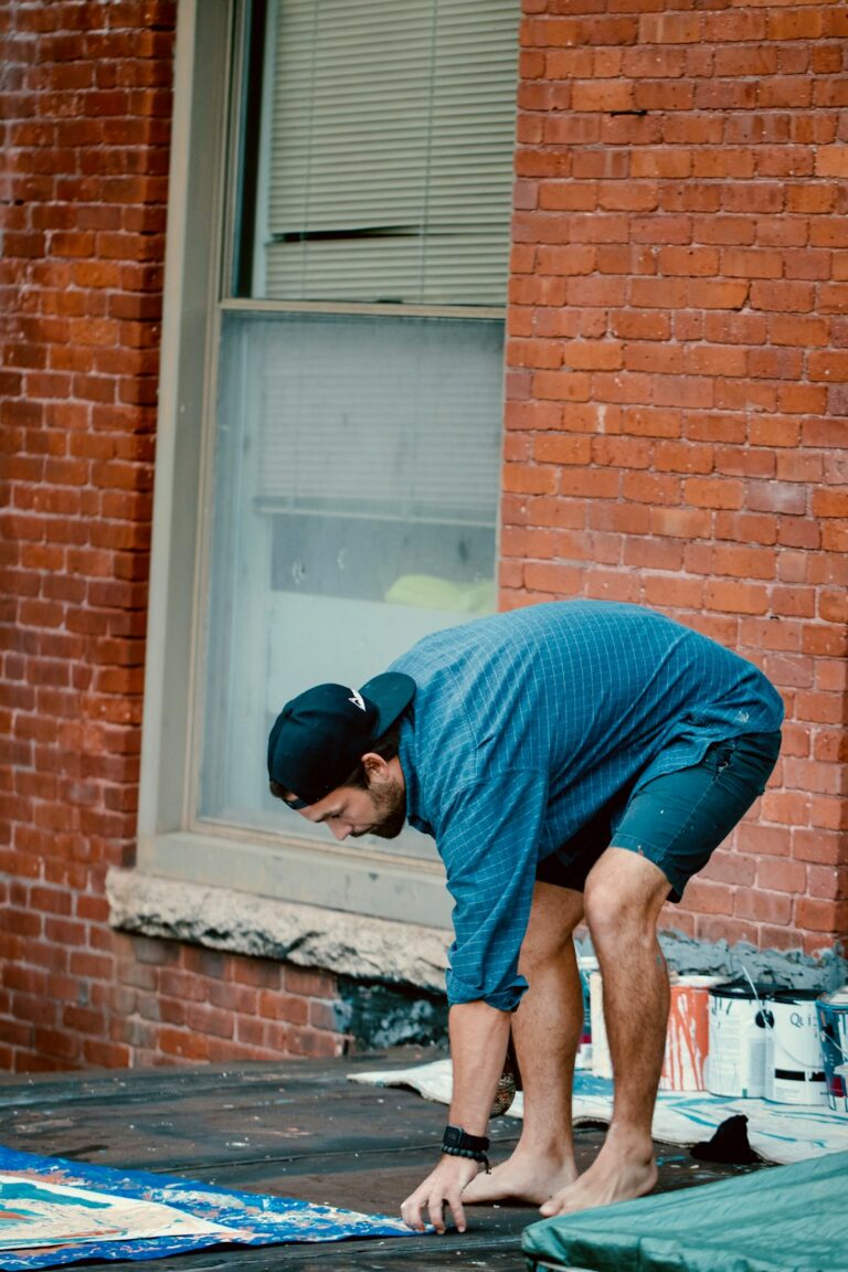 A masked worker examines a roof edge while a homeowner photographs water damage inside the home.